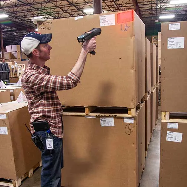 Warehouse worker scanning a large cardboard box with a handheld barcode scanner