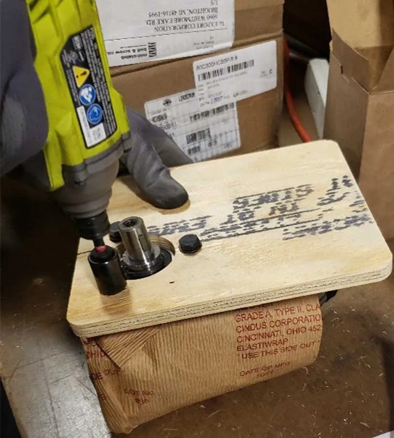  worker using a drill to secure military packages onto a wooden crate